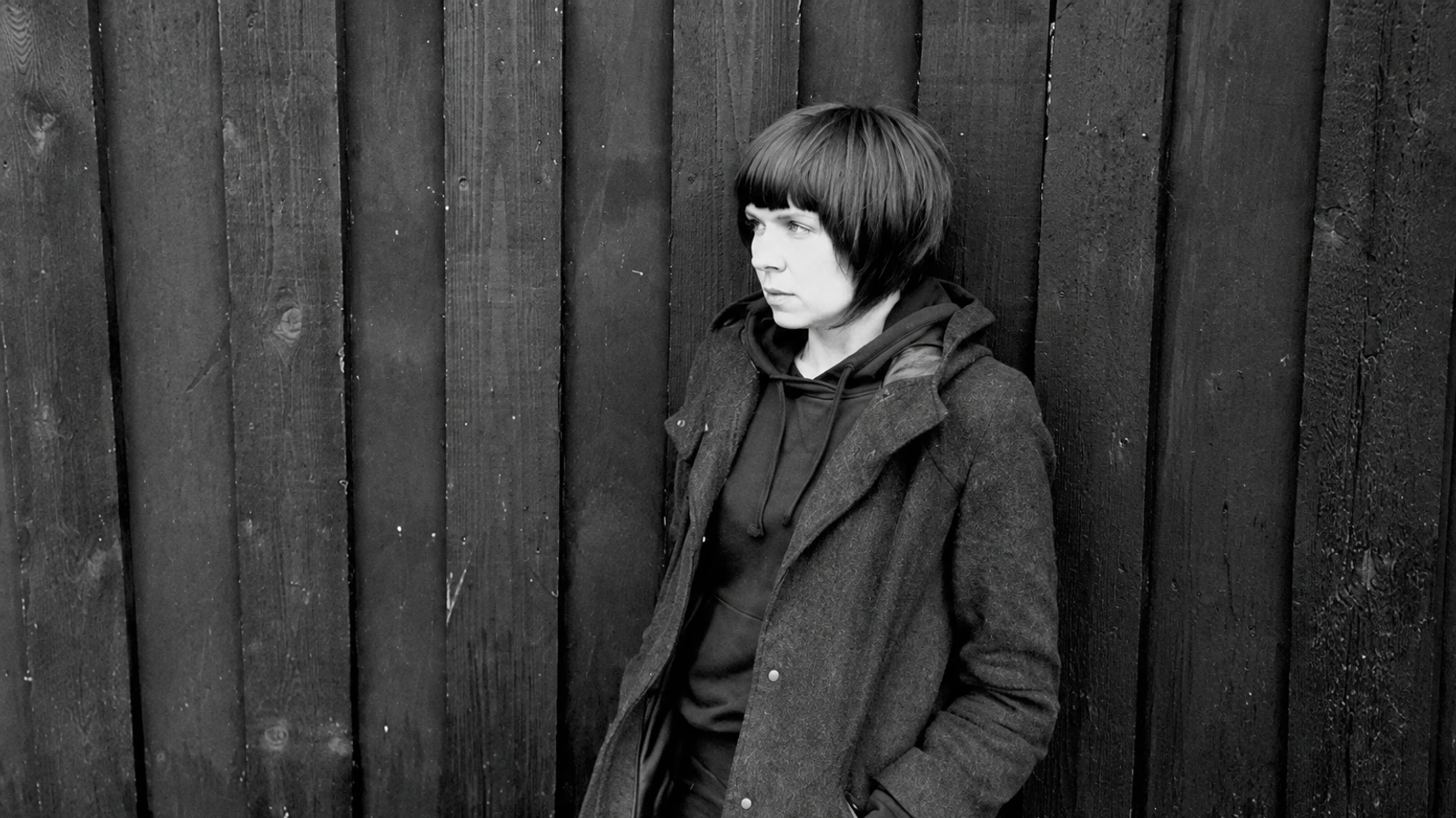 DJ Skirt in profile against a dark wooden wall.