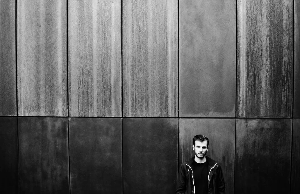 Gábor Lázár standing against a large textured industrial wall.