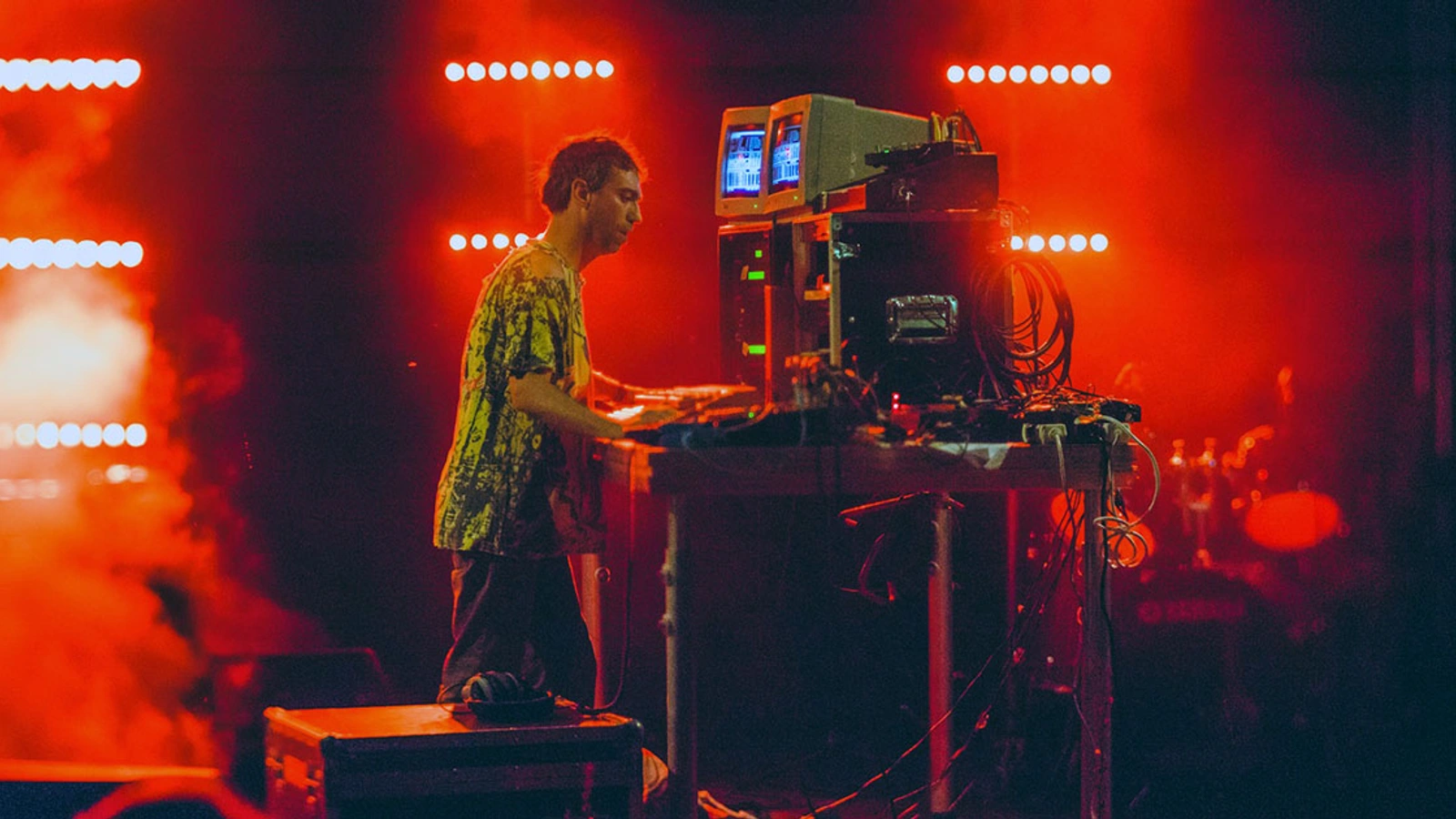Live performance at Braillė Satellitė under red stage light and smoke, with a musician and electronic equipment.