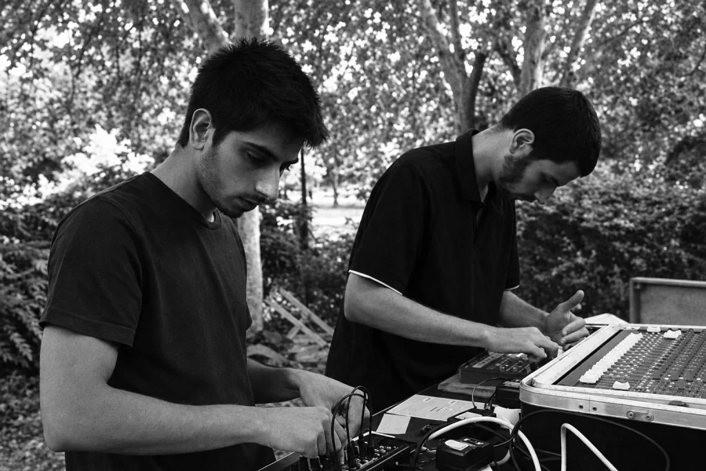 Sturqen performing outdoors with electronic instruments, in a monochrome photograph.