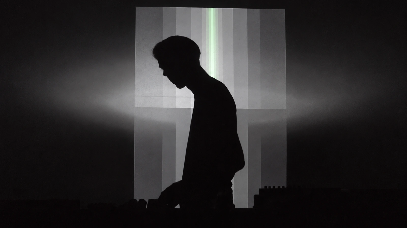 Senking performing in silhouette against an abstract projection of grey vertical bands.