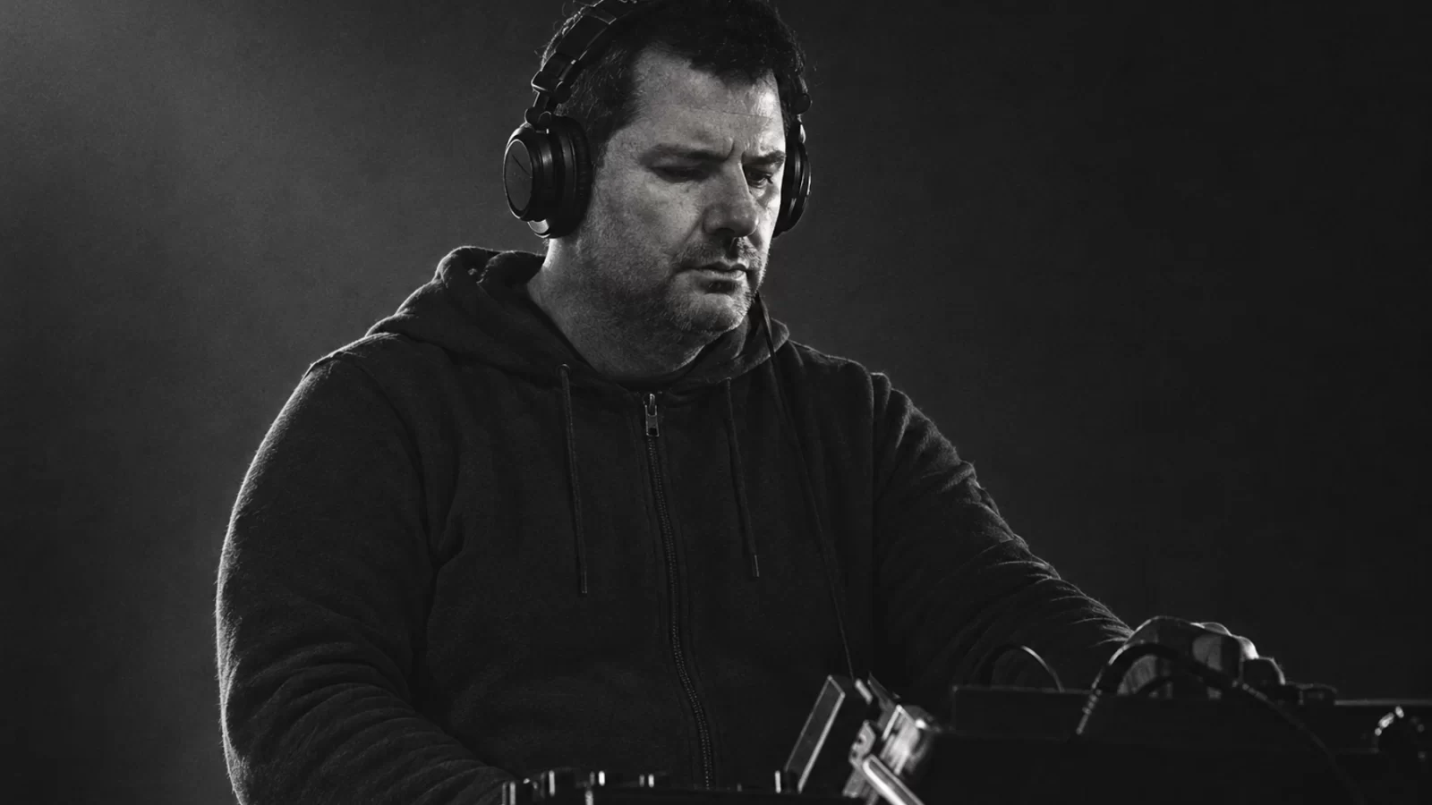 Mlada Fronta performing in black headphones and a dark hoodie against a subdued stage background.