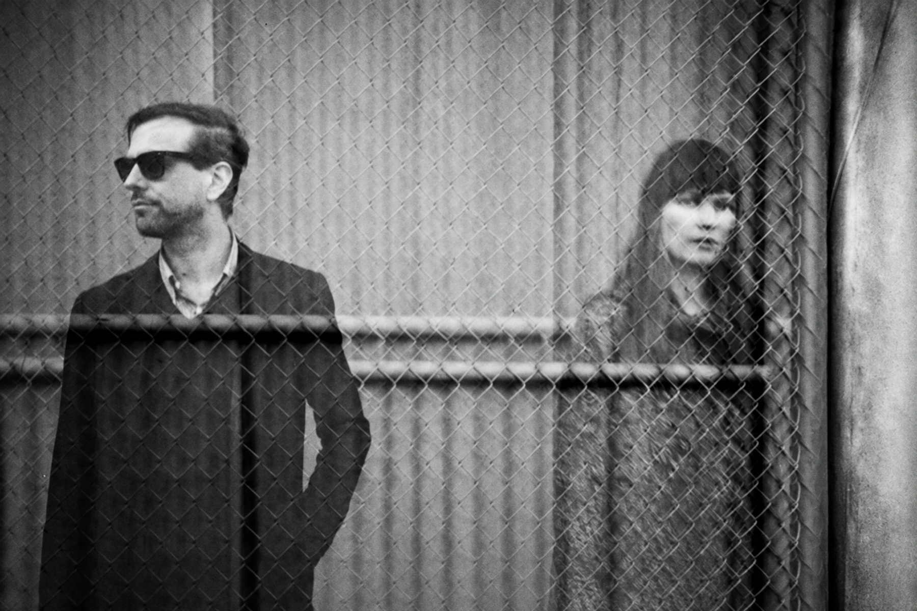 Xeno & Oaklander seen through a chain-link fence in a ghostlike double-exposure photograph.