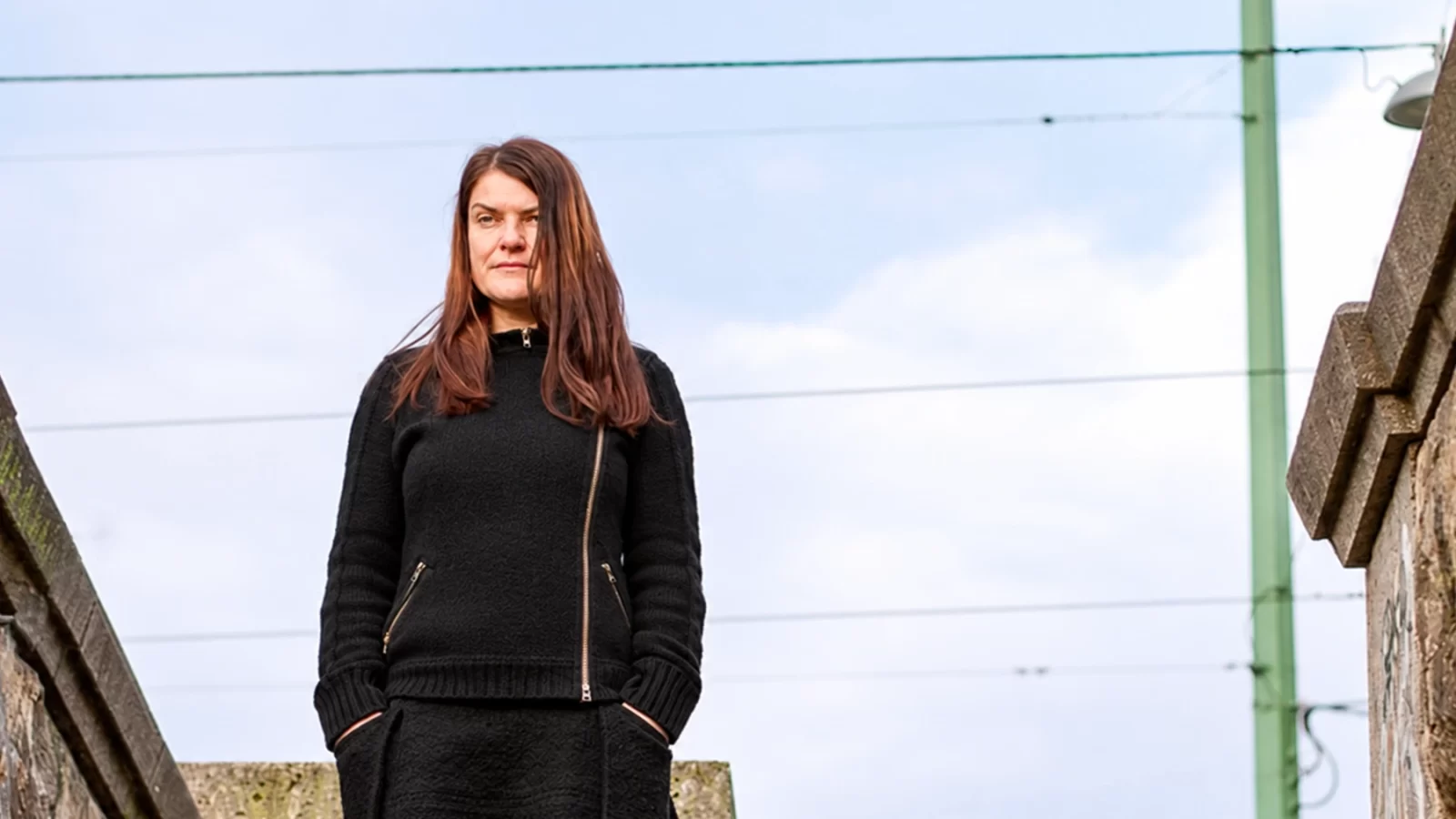 Chra in a black sweater standing on stone stairs.