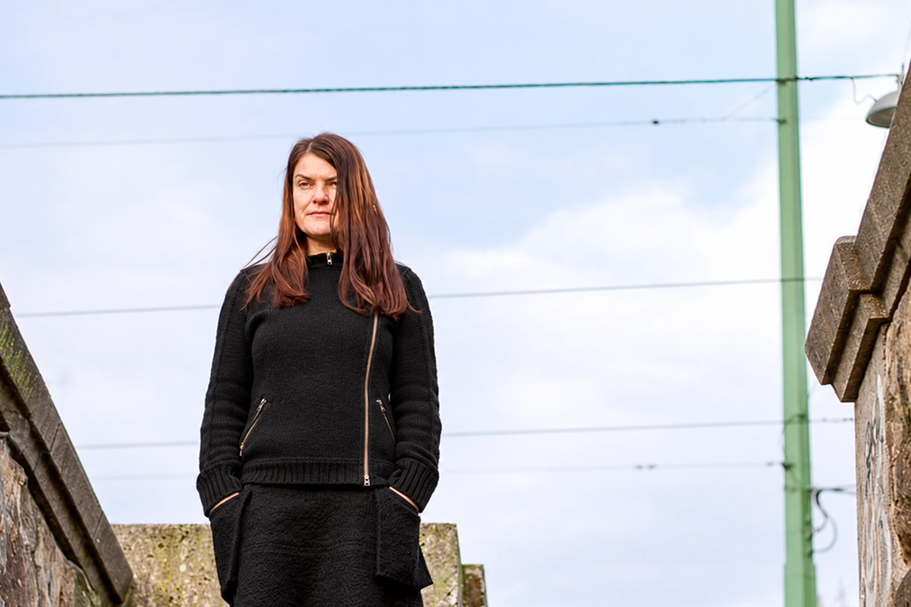Chra in a black sweater standing on stone stairs.