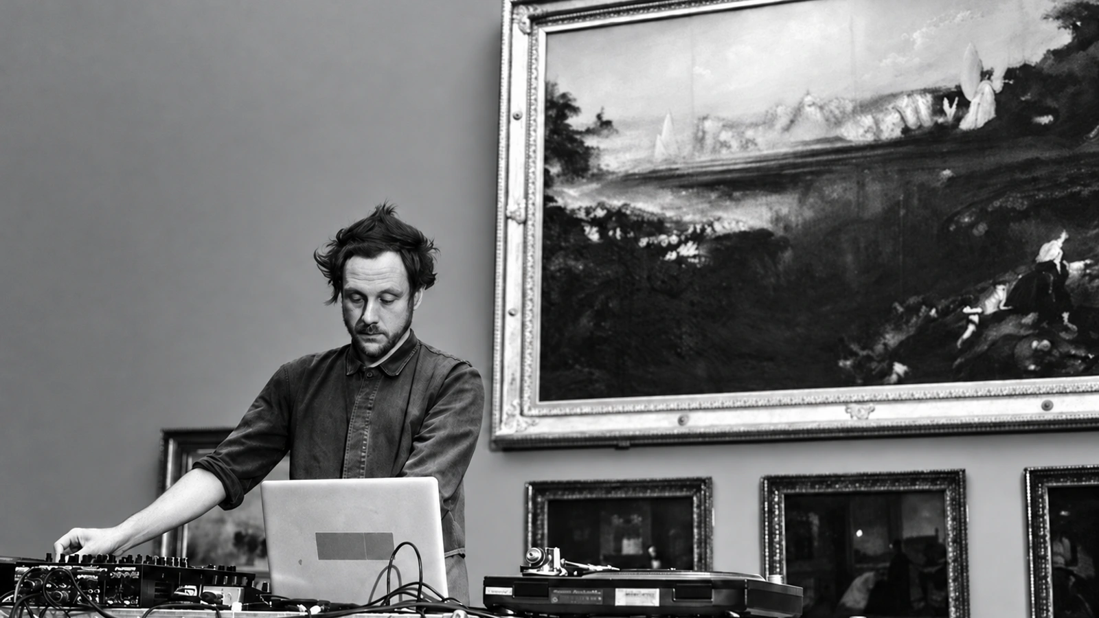 Lee Gamble performing at a table of electronic equipment in a gallery.