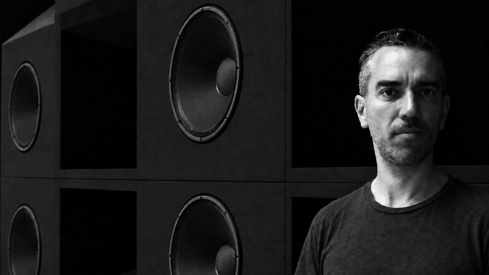 Robert Curgenven standing beside a wall of dark loudspeaker cabinets.