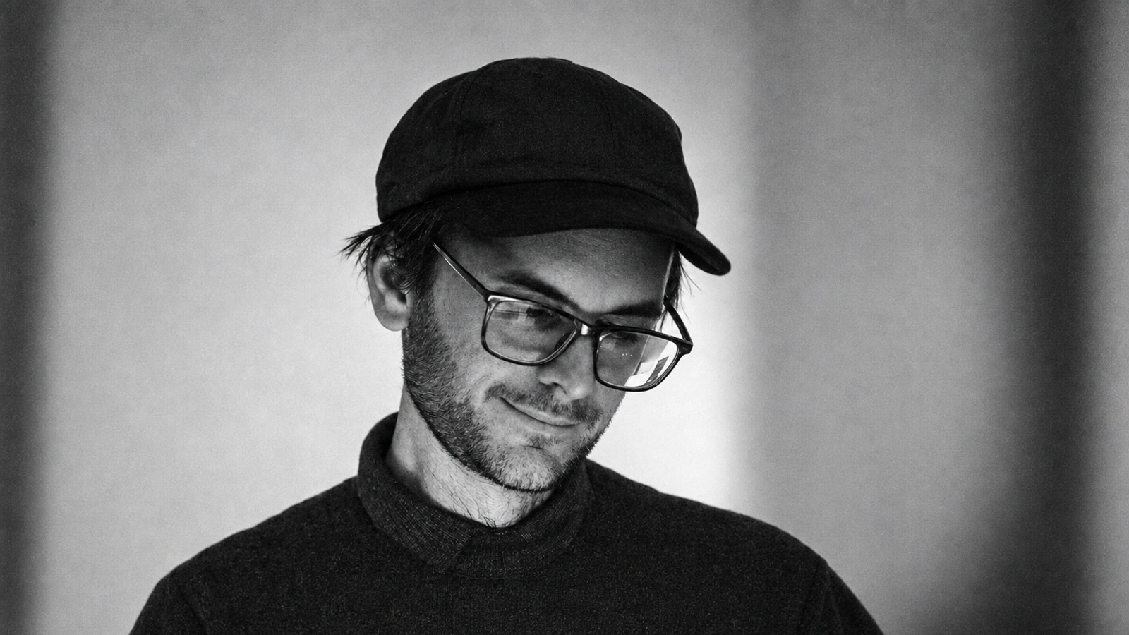 Ben Vida in a black cap, glasses and dark sweater, looking down.