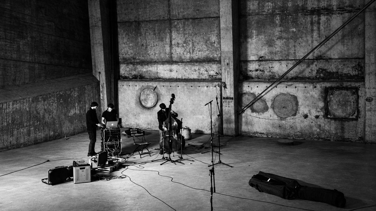 Three musicians with double bass, electronics and microphones in the industrial interior of Kraftwerk, Berlin.