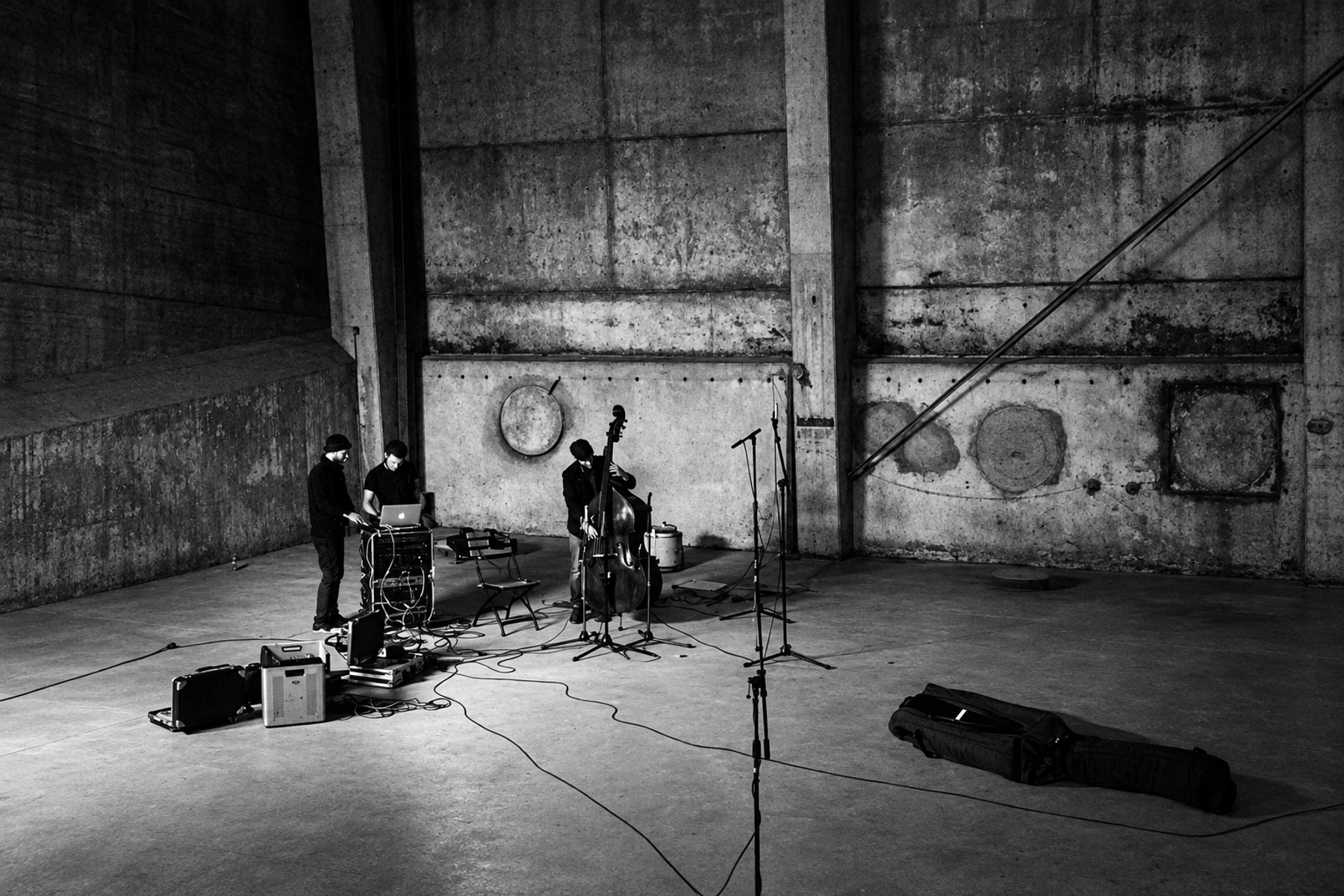 Three musicians with double bass, electronics and microphones in the industrial interior of Kraftwerk, Berlin.