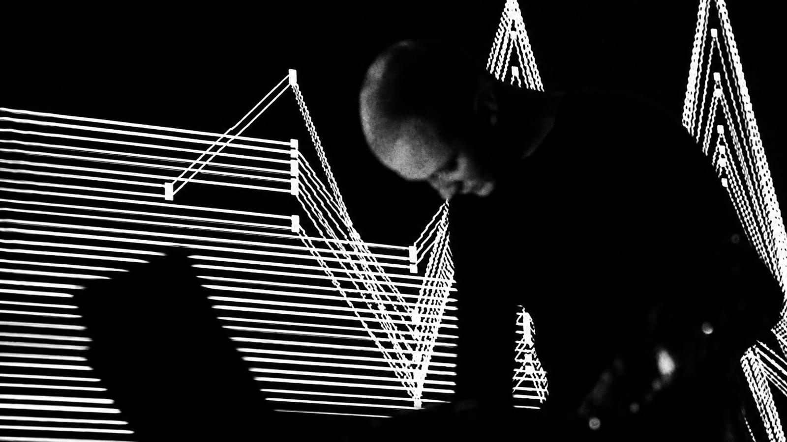 Kangding Ray performing in silhouette against intersecting white projected lines.