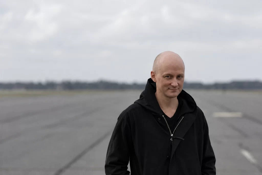 Kangding Ray in a dark jacket in an open landscape under an overcast sky.