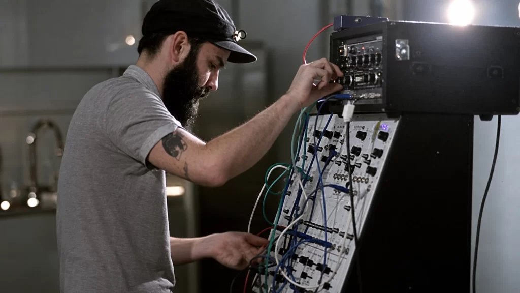 Peder Mannerfelt in profile adjusting a modular synthesizer during a live performance.