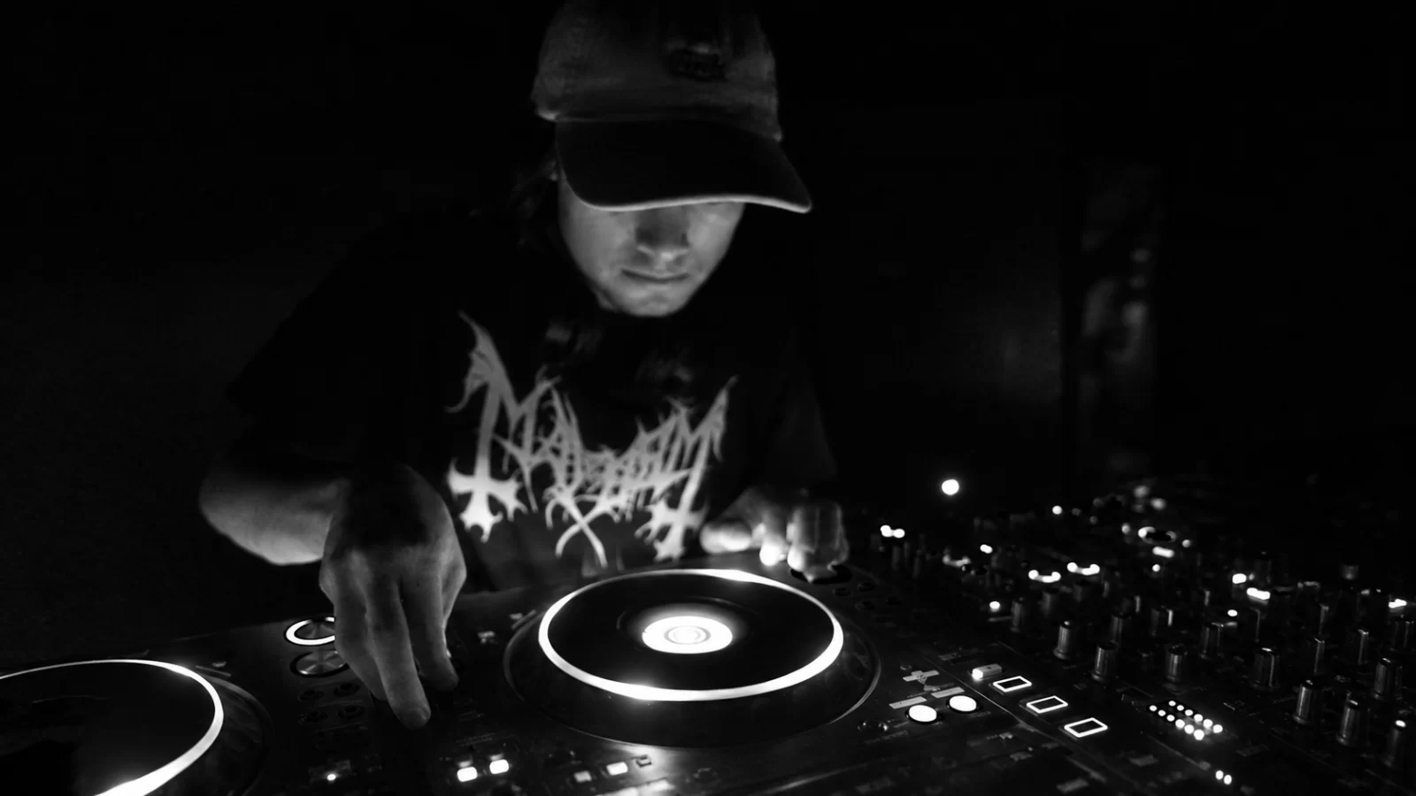 UNKNOWN performing at a DJ console in a dark black-and-white photograph.