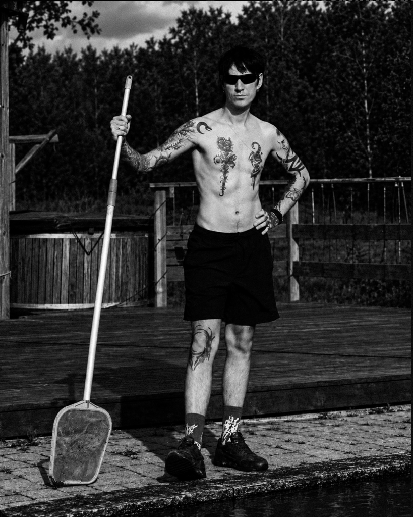 Justinas / S13 holding a pool net while cleaning the pool in the countryside, in a black and white photograph.
