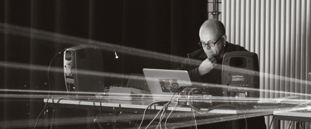 Robert Henke seated behind a laptop, speakers and laser equipment in Berlin in 2013