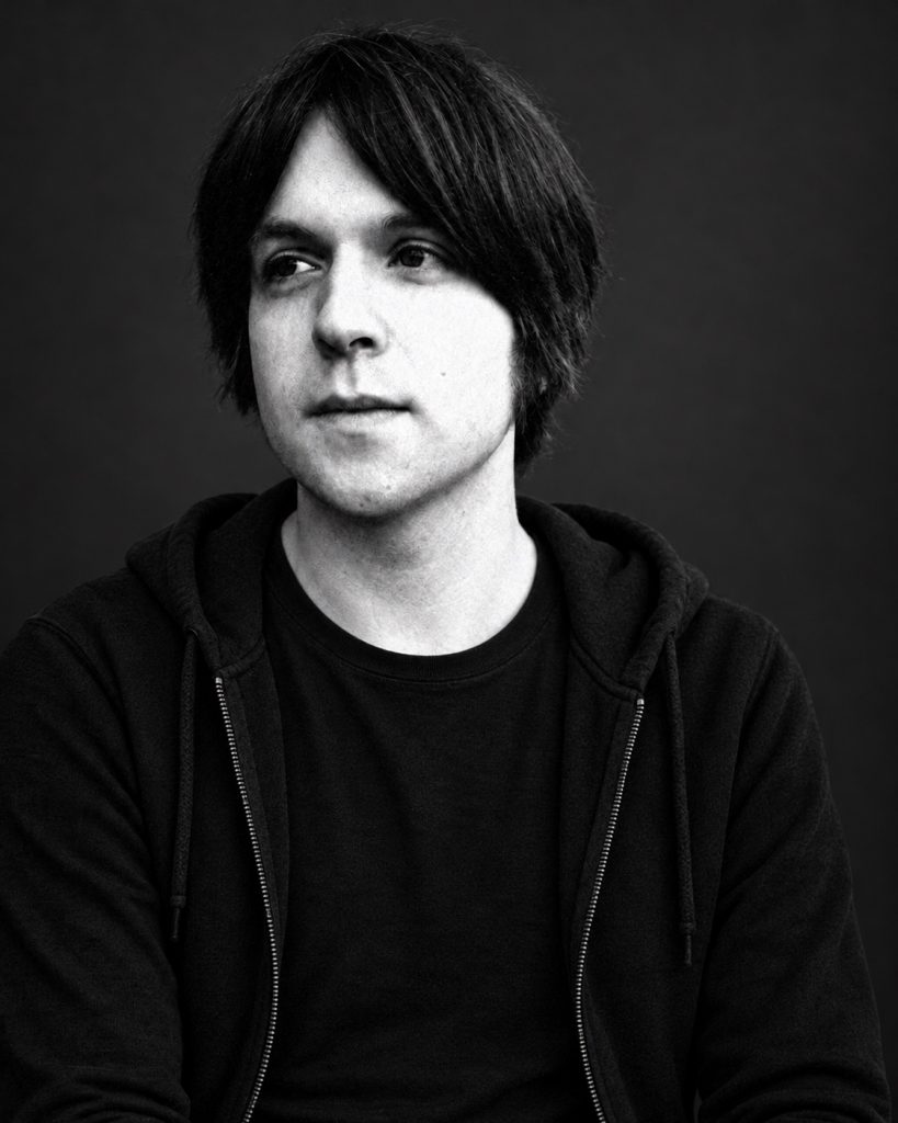 James Blackshaw in a black hooded sweatshirt — restored editorial portrait