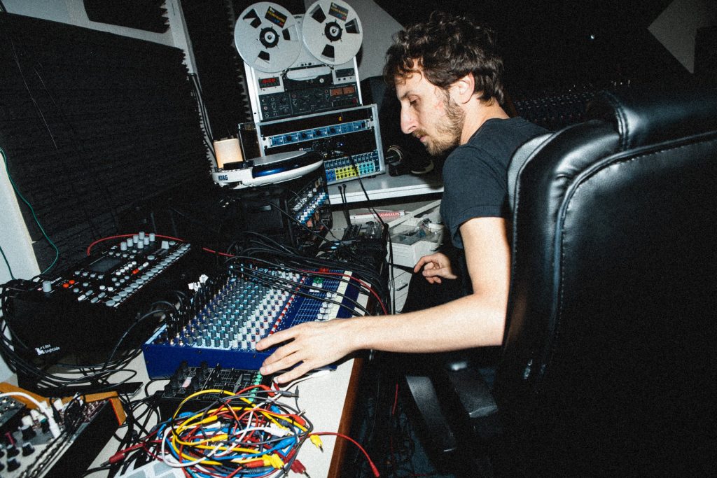 Lucy at the mixing console in his home studio, surrounded by electronic instruments and a reel-to-reel recorder