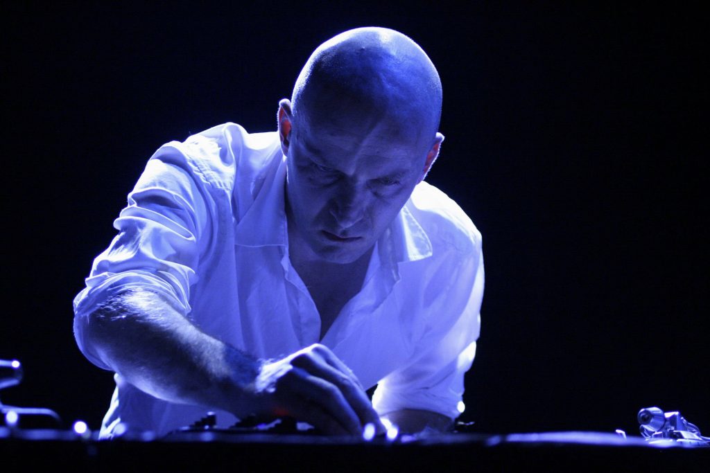Franck Vigroux adjusting electronic instruments while performing under blue light