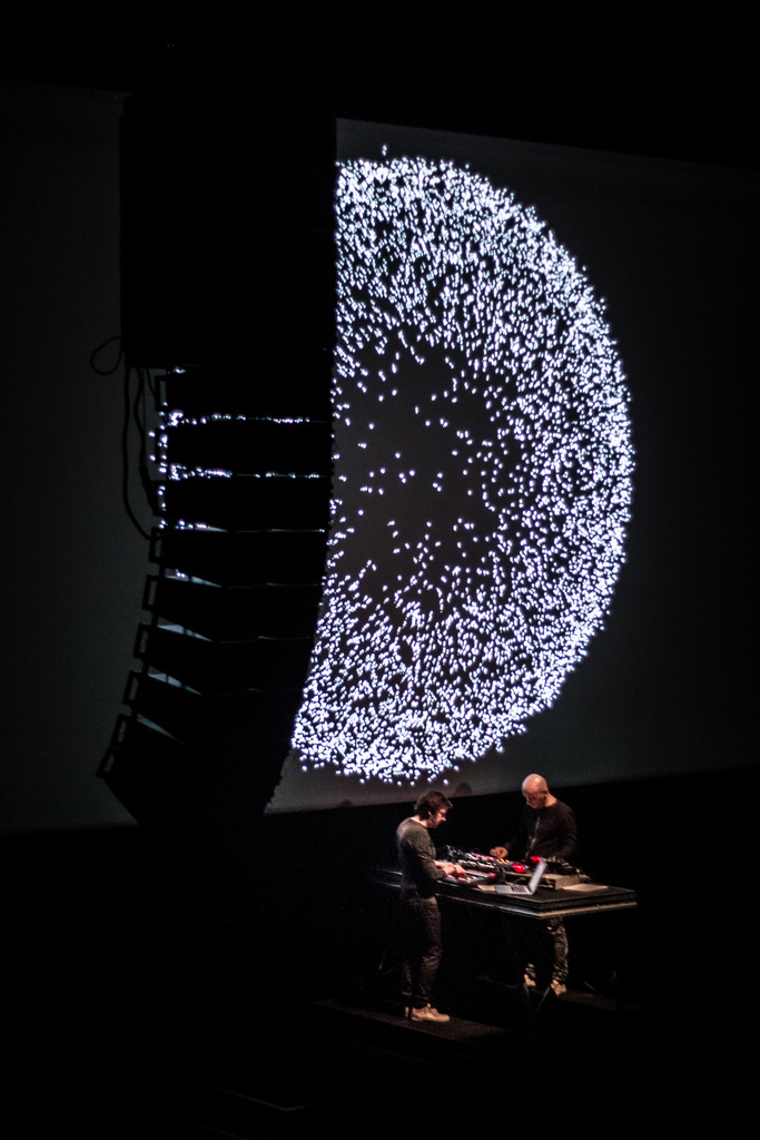 Franck Vigroux and Antoine Schmitt performing Tempest beneath a large projection of particles