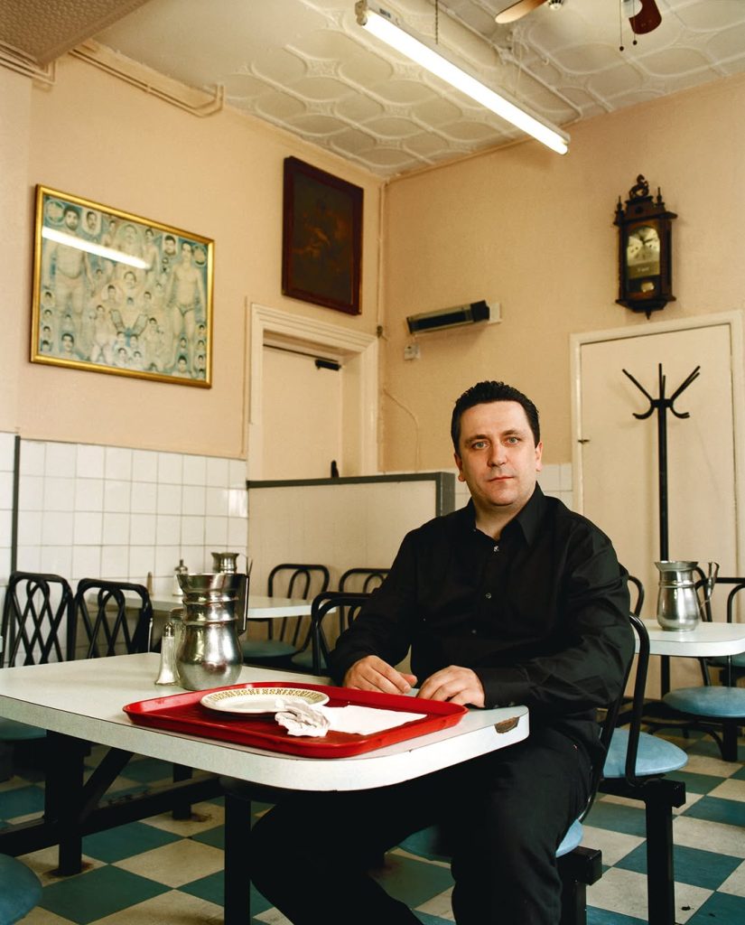 Peter Rehberg seated at a table in Sweet & Spicy, wearing a black shirt, with a red tray and metal teapots.