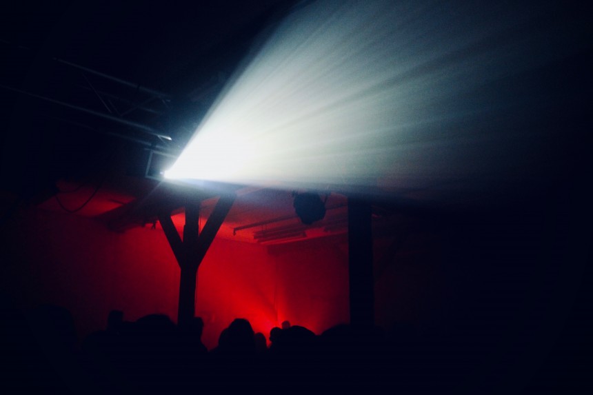 Audience silhouettes beneath a projector beam at Mayhem.