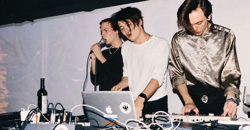 Three musicians performing with a microphone and electronic equipment.